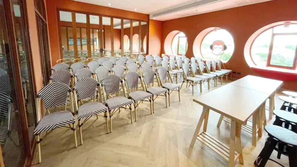 Rows of patterned chairs facing tables in an orange meeting room with round windows at Blu Monkey Hub & Hotel Bangsaen