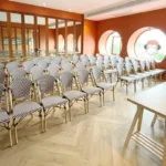 Rows of patterned chairs facing tables in an orange meeting room with round windows at Blu Monkey Hub & Hotel Bangsaen