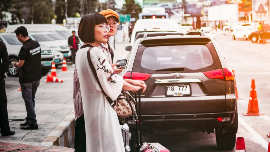 Travellers preparing luggage beside a parked car in Thailand