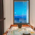 Illustrative bathtub beside a window overlooking the sea